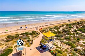Een strand met een redershut, mensen op het strand en een helder uitzicht over de oceaan.