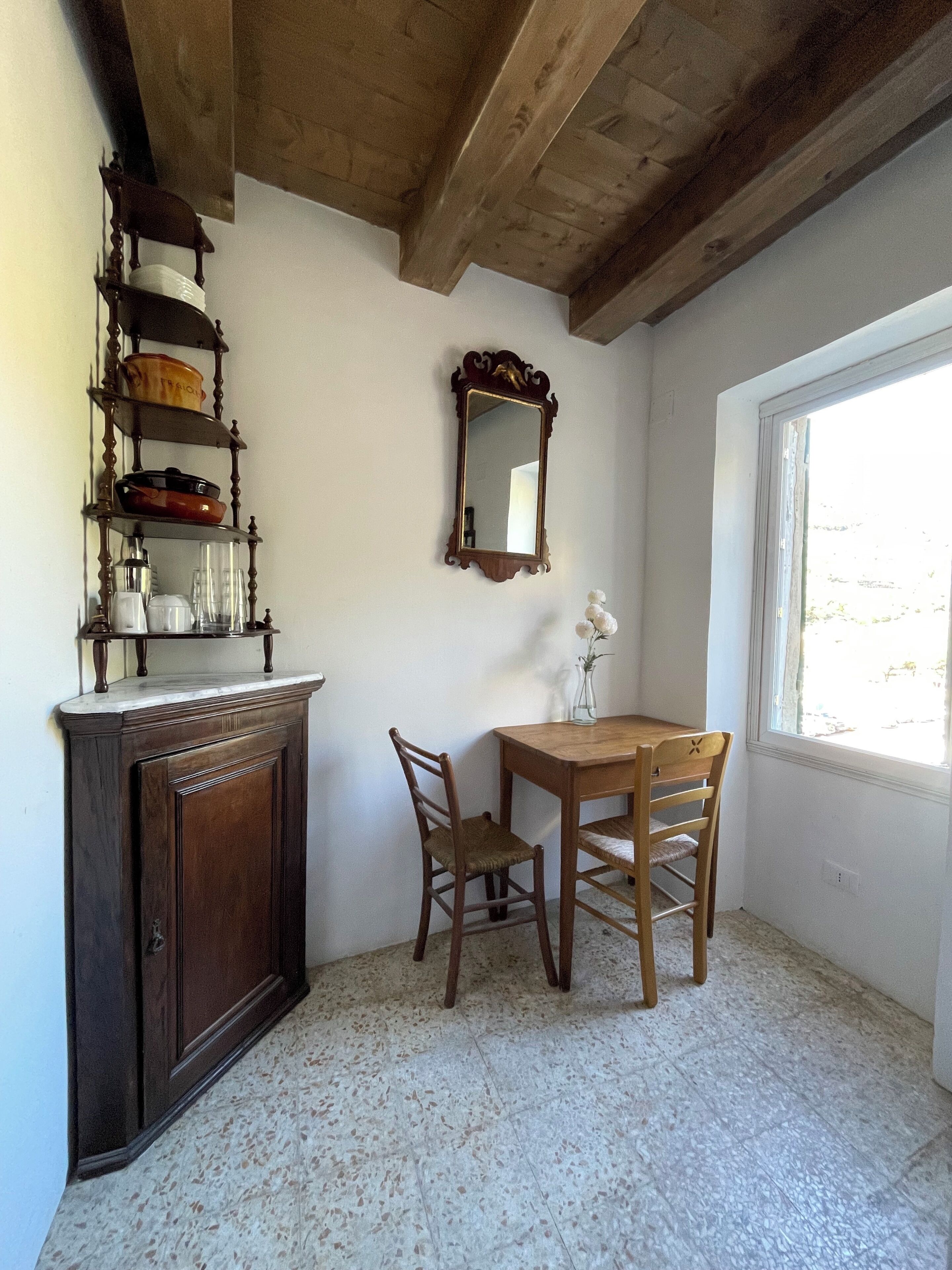 A dining area with a wooden table and chairs, a cabinet with dishes, a mirror, and a window with a view.