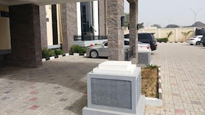 A parking area with a covered walkway, stone pillars, and a row of parked cars. - Global Luxury Suites (Kano)