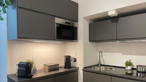 A modern kitchen with dark cabinets, a stainless steel sink, a kettle, and a coffee machine.