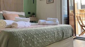 A bedroom with a bed, pillows, a bedside table, a hanging light, and two framed pictures on the wall.