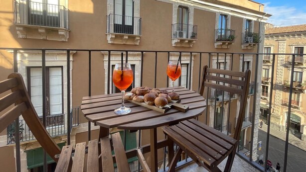 A balcony with a wooden table, two glasses of red drink, and a plate of pastries.