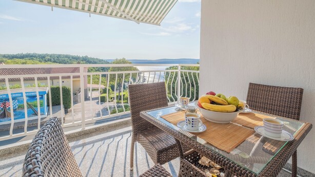 Ein Balkon mit Korbmöbeln, einem Glastisch und einer Obstschale.