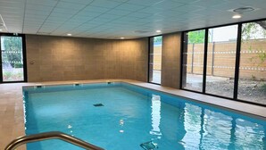 An indoor swimming pool with clear blue water, tiled walls, and large windows offering views of the outdoors. - Nemea Appart Hotel Strasbourg Illkirch (Illkirch-Graffenstaden)