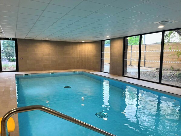 An indoor swimming pool with clear blue water, tiled walls, and large windows offering views of the outdoors. - Nemea Appart Hotel Strasbourg Illkirch (Illkirch-Graffenstaden)