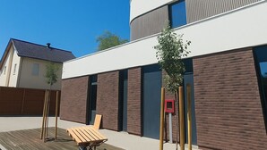 A modern building with a flat roof, a wooden deck with a bench, and a small tree. - Nemea Appart Hotel Strasbourg Illkirch (Illkirch-Graffenstaden)