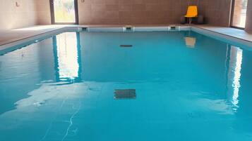 An indoor swimming pool with clear water, tiled walls, and a bright ceiling.