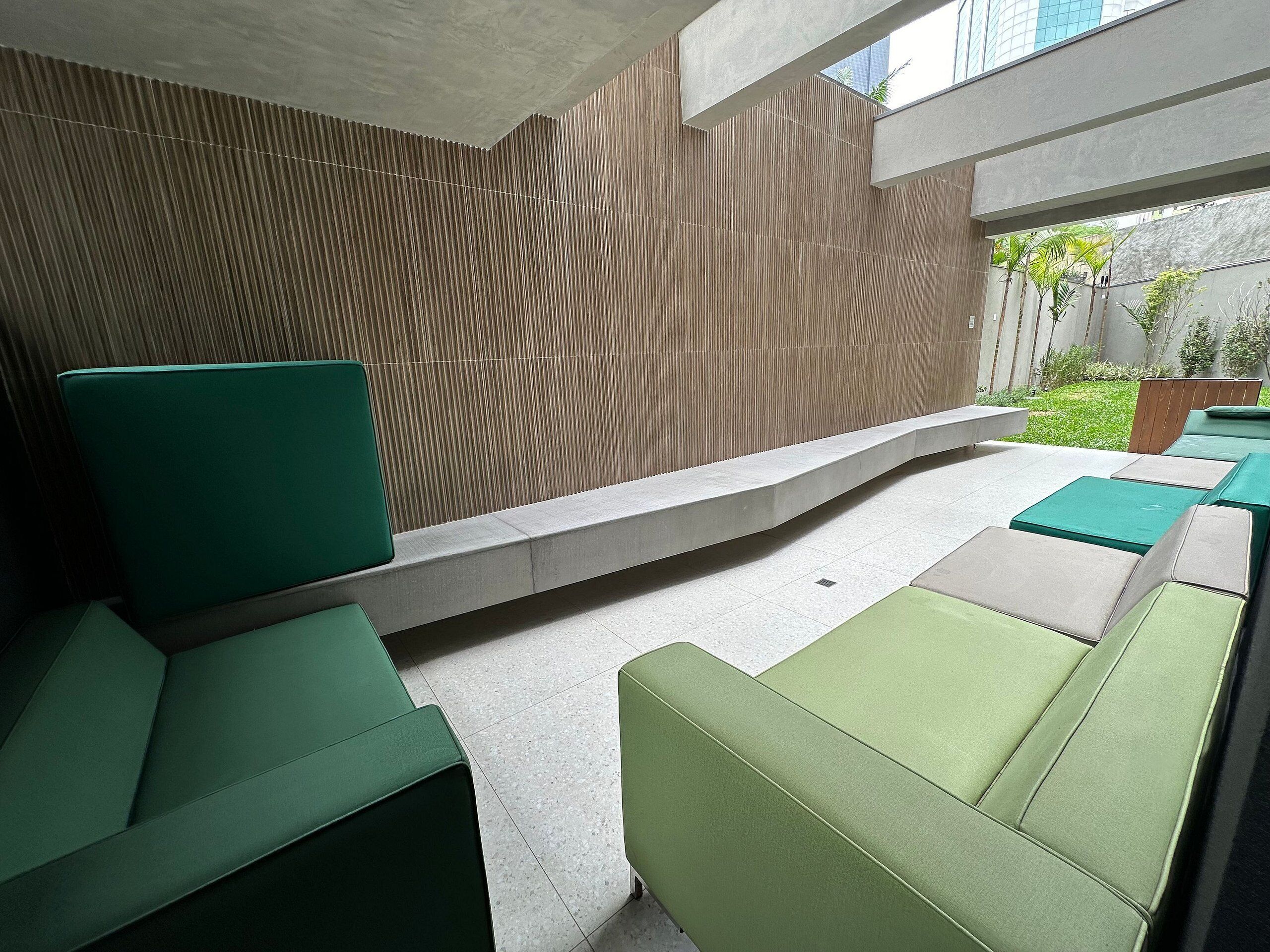 A modern outdoor seating area with green cushioned chairs and a concrete bench.