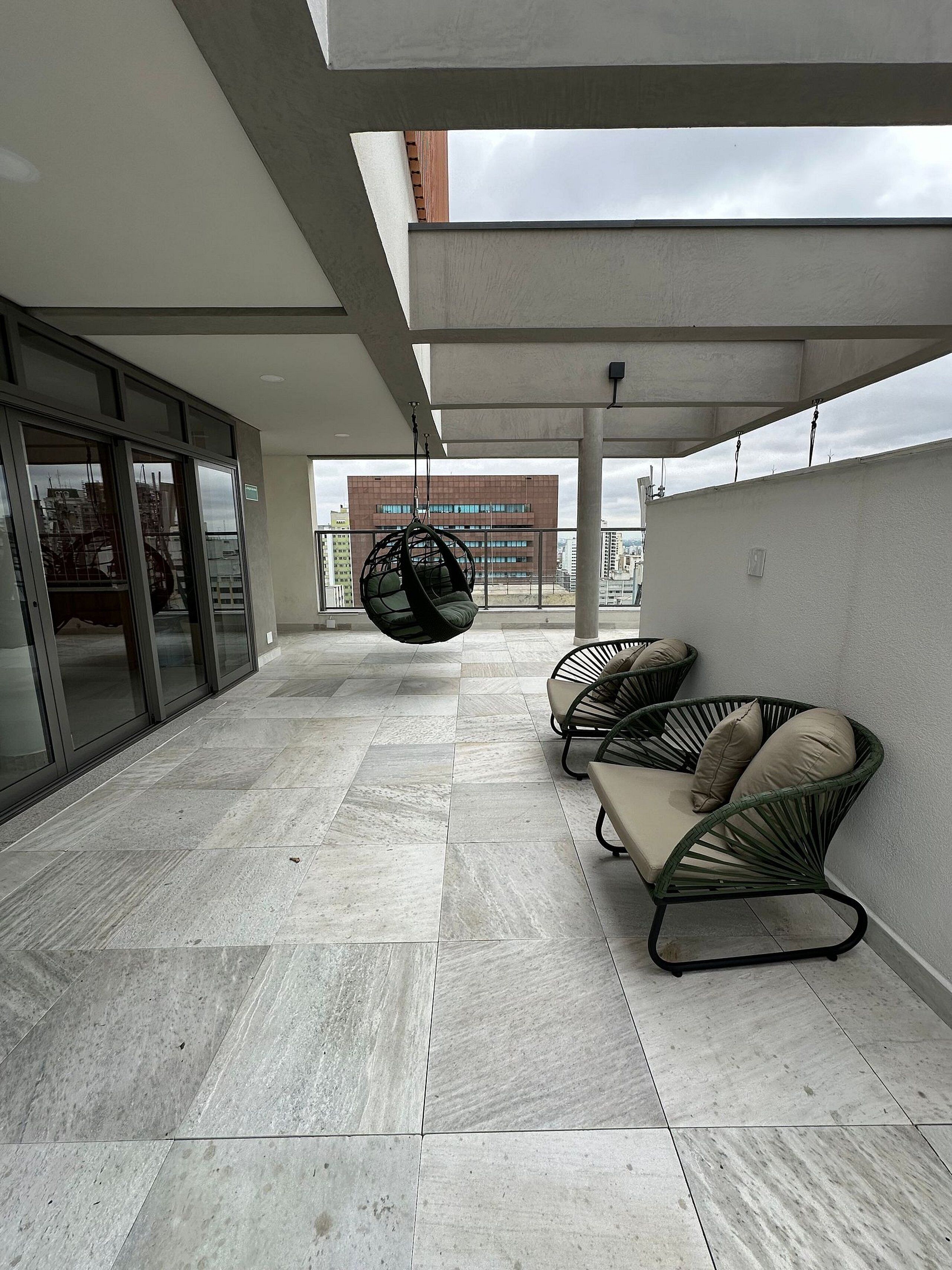 A spacious balcony with a hanging chair, cushioned chairs, and a view of a building in the background.