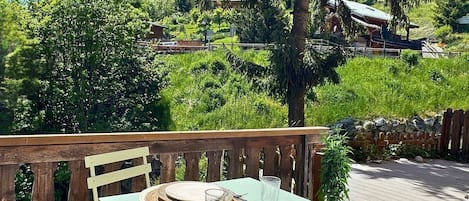 An outdoor dining area with a table set for two, overlooking a scenic landscape with trees and a distant building.