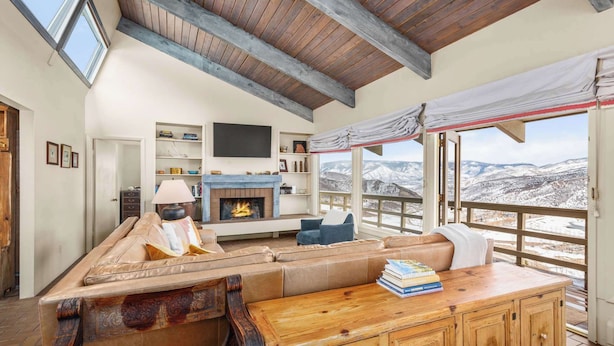 Un salon chaleureux avec une cheminée, un canapé en cuir et une vue sur des montagnes enneigées.