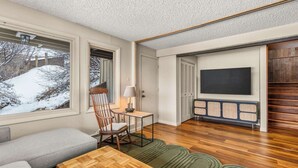 Un salon chaleureux avec un canapé, une table basse en bois, un fauteuil, un téléviseur et un meuble de rangement intégré pour les appareils multimédias.