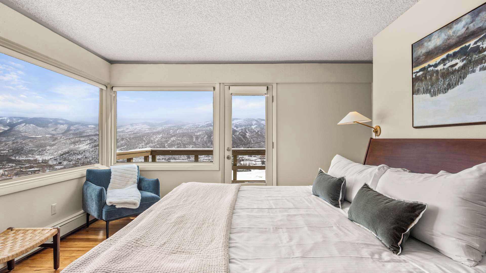 Quarto com uma cama grande, uma cadeira, vista para montanhas nevadas e um quadro na parede.