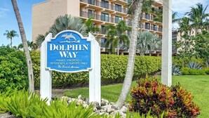 Señal de Dolphin Way que indica propiedad privada sin acceso a la playa, rodeada de vegetación exuberante y un edificio de varios pisos al fondo.