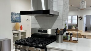 Una cocina moderna con estufa de acero inoxidable, armarios blancos y una campana extractora negra.
