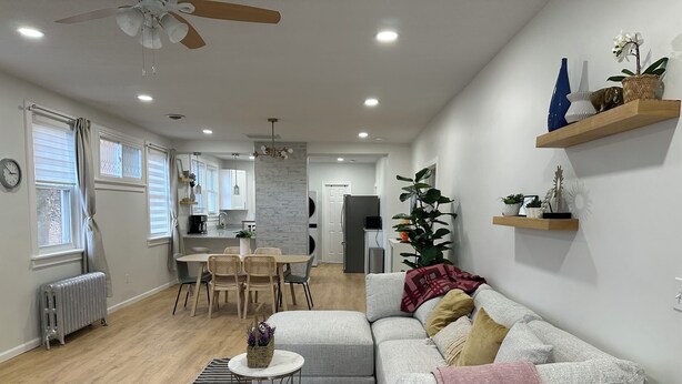 Una sala moderna con un sofá gris, una mesa de centro y un tapete a rayas. Se aprecia una zona de comedor con una mesa y sillas, y una cocina al fondo.