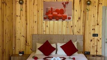 Un dormitorio con paneles de madera, una cama, almohadas rojas, una disposición de toallas en forma de corazón y una lámpara fijada a la pared.