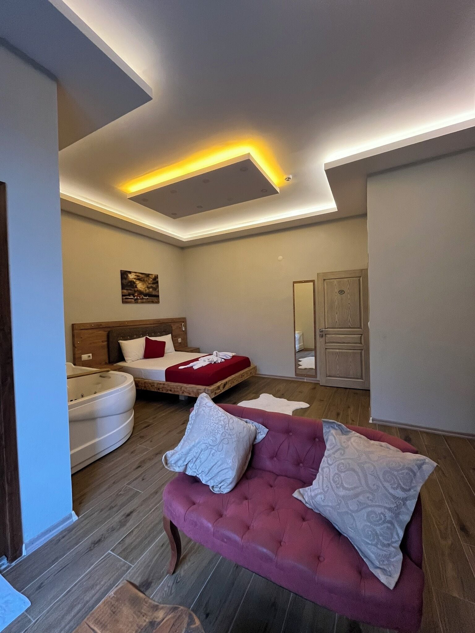 A modern bedroom with a bed, a red sofa, a white bathtub, and a wooden floor.