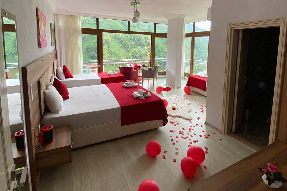 Une chambre spacieuse avec un grand lit, un coin salon avec une table et des chaises, et une vue sur la verdure grâce à de grandes fenêtres.