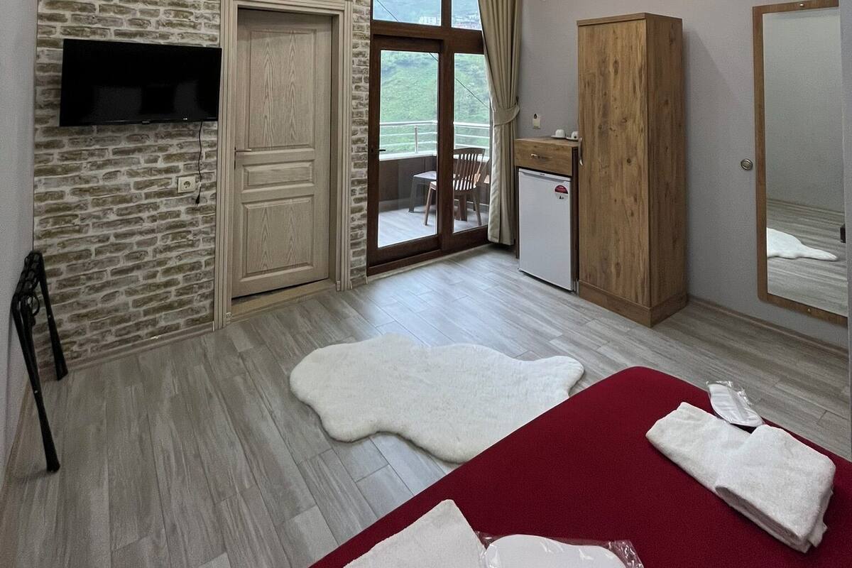 Une chambre d’hôtel moderne avec un mur en pierre, un téléviseur à écran plat, une armoire en bois, un grand miroir et un balcon avec vue.