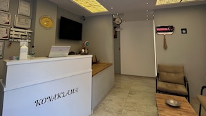 Un área de recepción con diseño moderno, que cuenta con un techo con diseño, un mostrador de recepción identificado como “KONAKLIMA” y un espacio de descanso con una mesa y sillas de madera.