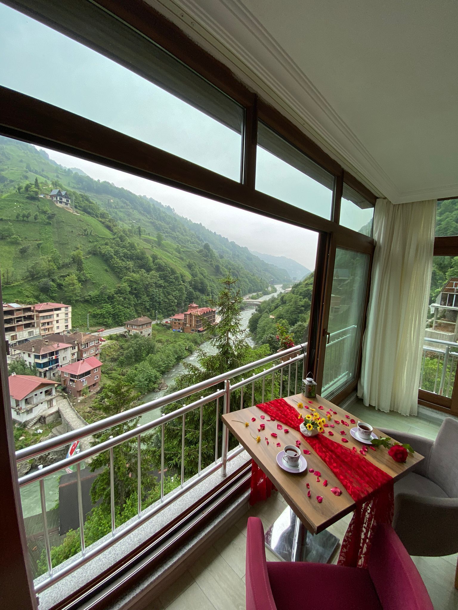 A balcony with a table set for two, overlooking a river and green hills.