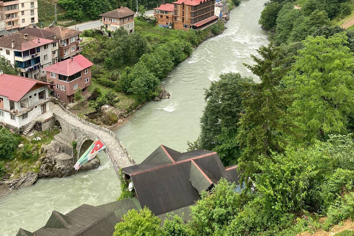 Une rivière traverse une vallée bordée de bâtiments, dont une construction remarquable se distingue par son toit rouge.