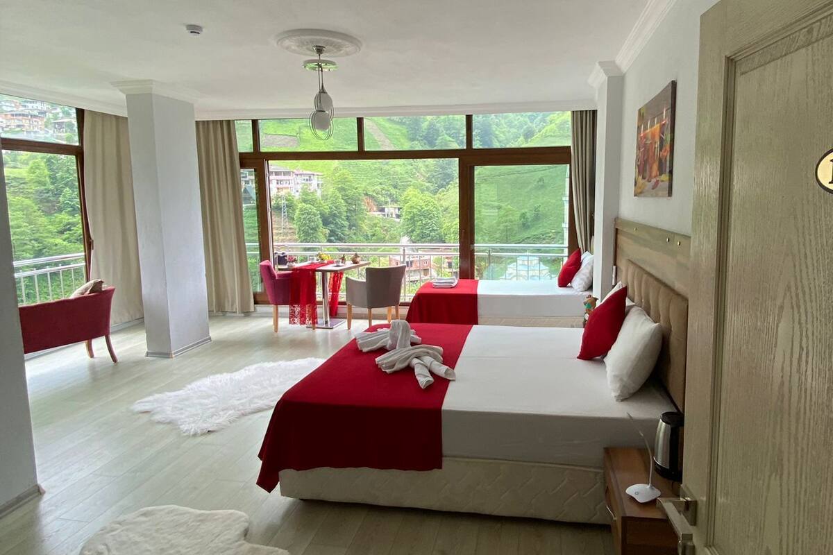 Une chambre spacieuse avec un grand lit, une vue sur la verdure et un balcon équipé d’une table et de chaises.