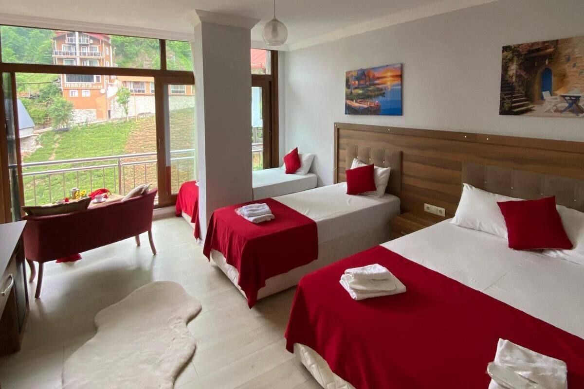 Une chambre d’hôtel avec deux lits, une tête de lit en bois, une grande fenêtre donnant sur un beau paysage, une petite table et un tapis rouge.