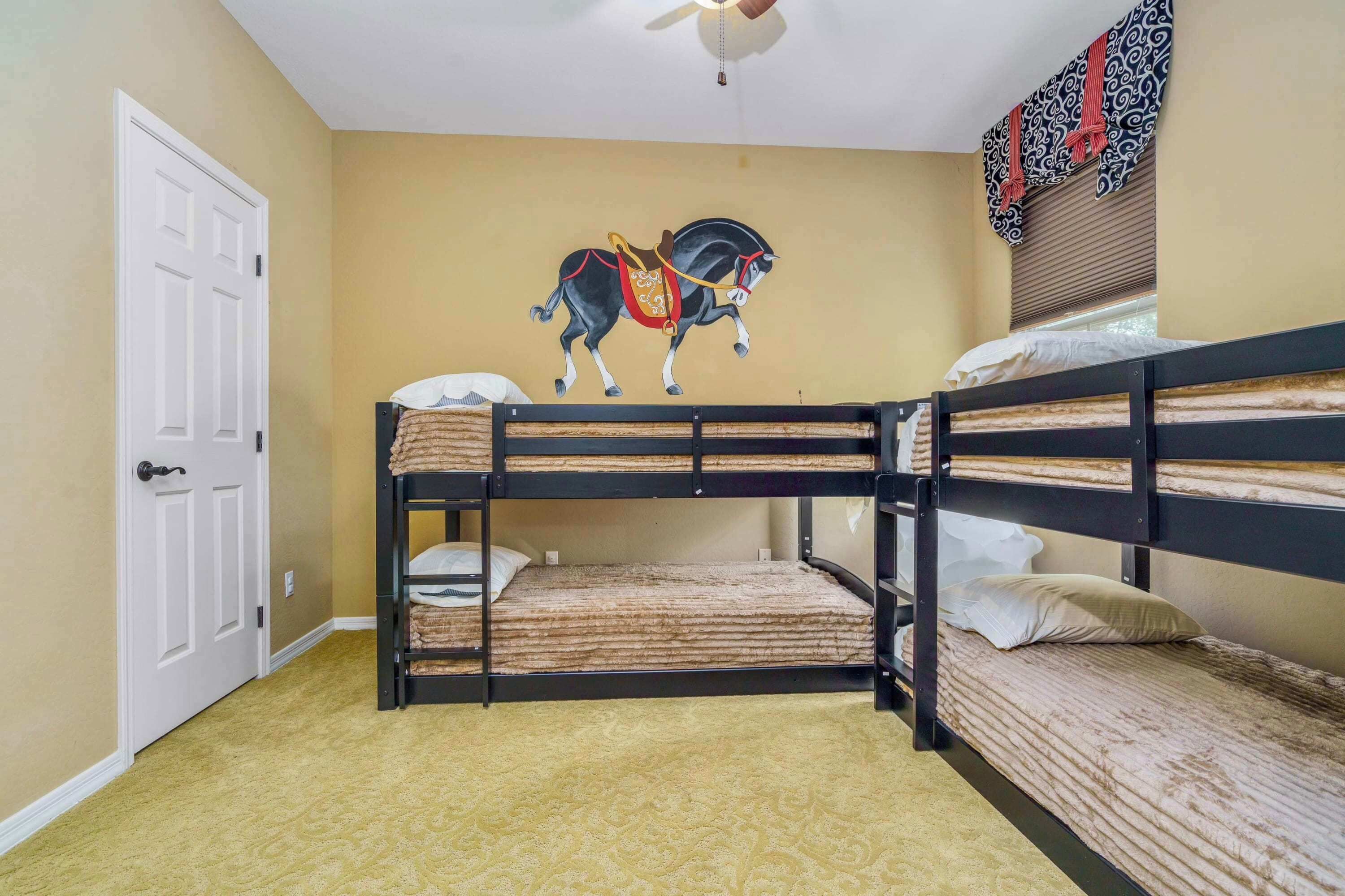 Une chambre avec un lit superposé, un ventilateur de plafond, une porte et une fresque murale représentant un cheval.
