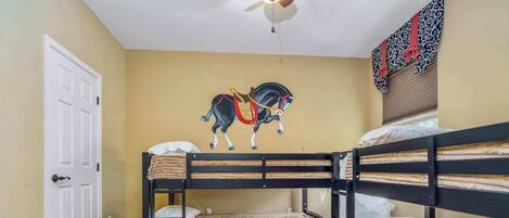 Une chambre avec un lit superposé, un ventilateur de plafond, une porte et une fresque murale représentant un cheval.