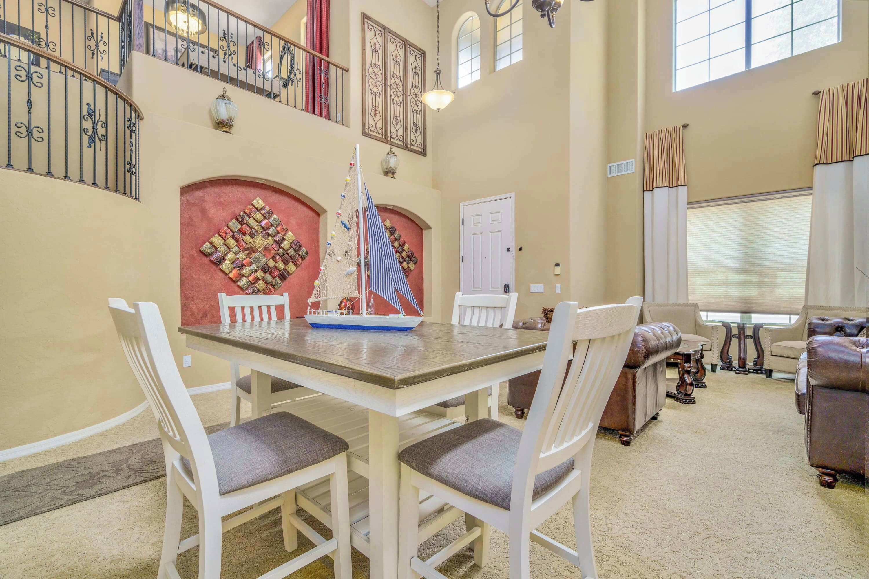 A spacious living area with a dining table, white chairs, a sofa, and a staircase with ornate railings.