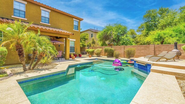 A clear swimming pool with a tiled deck, surrounded by a brick wall and palm trees. - Pool, Movie Room, Games, Grill! (Goodyear)