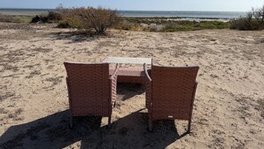 A beach setting with two wicker chairs and a table, facing the ocean.