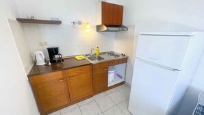 A compact kitchen with wooden cabinets, a white refrigerator, a coffee maker, and a sink. - Apartman Kate 2 (Dramalj)
