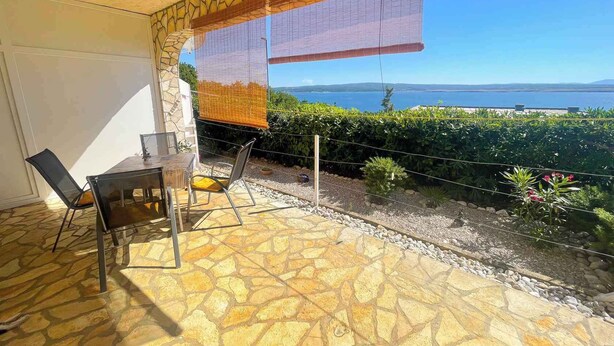 A patio with a stone floor, a table, two chairs, and a view of the sea. - Apartman Kate 2 (Dramalj)