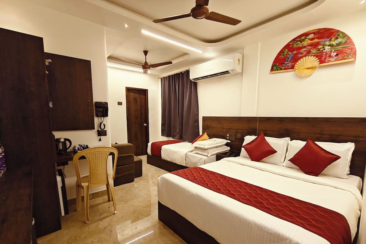 A hotel room with two beds, a desk, a chair, an air conditioning unit, a ceiling fan, and a decorative wall hanging.