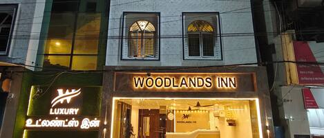 Un hotel llamado "Woodlands Inn" con un letrero, una recepción y un área de estar visible a través de la entrada.