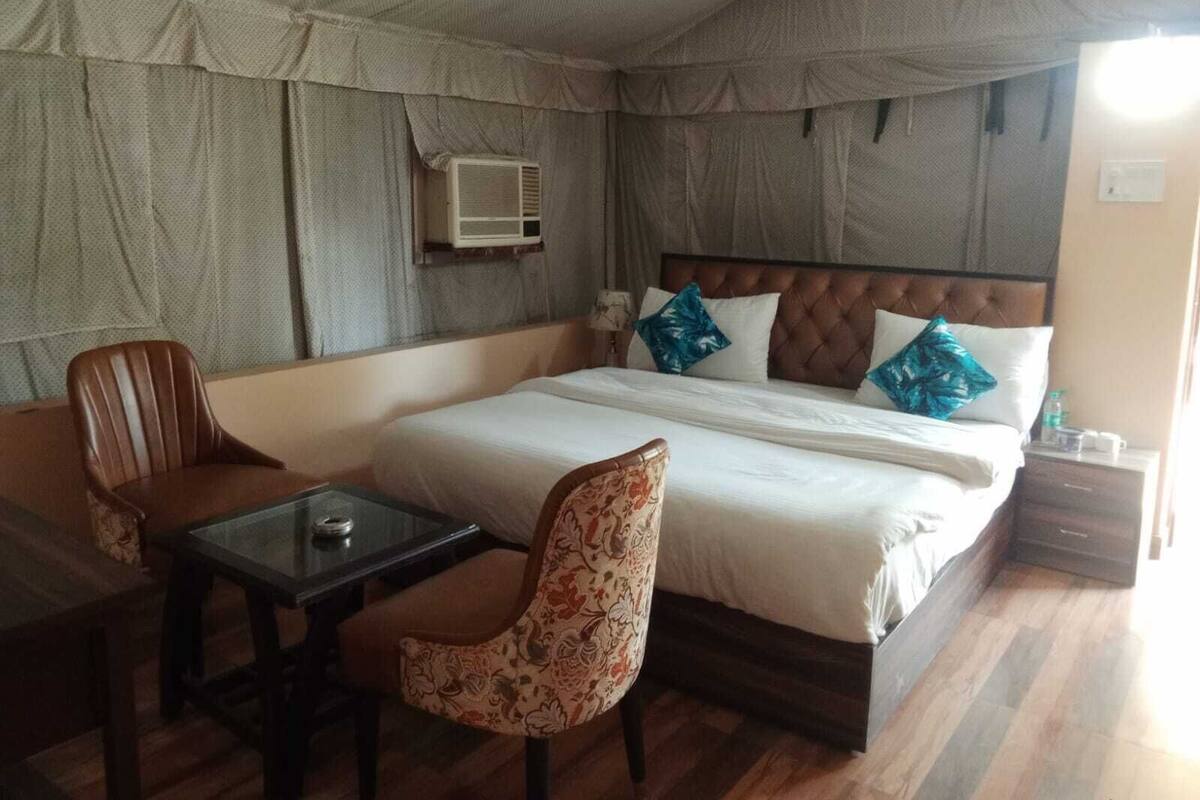 Un dormitorio con cama, una mesa, dos sillas, un equipo de aire acondicionado y una mesita de noche.