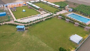 An aerial view of a resort with multiple buildings, a swimming pool, and a large lawn area. - MST Farm & Resort (Ghaziabad)