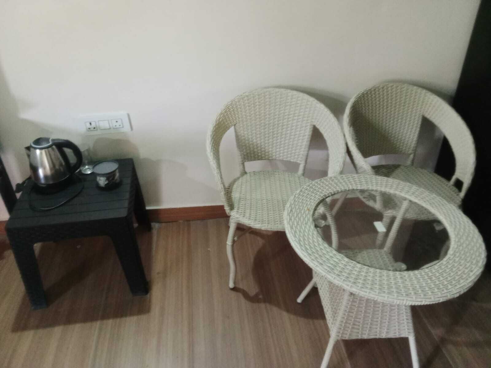 A room with a small table, two wicker chairs, a kettle, and a cup.