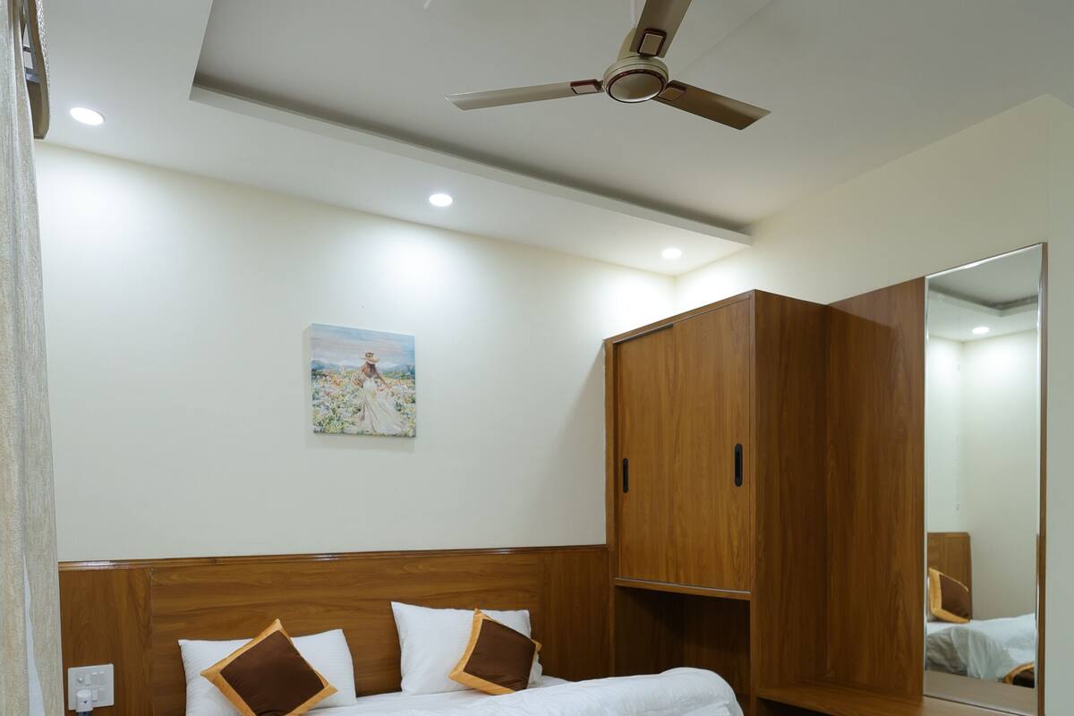 Un dormitorio moderno con una cama de madera, un ventilador de techo, un espejo grande y una mesita de noche.