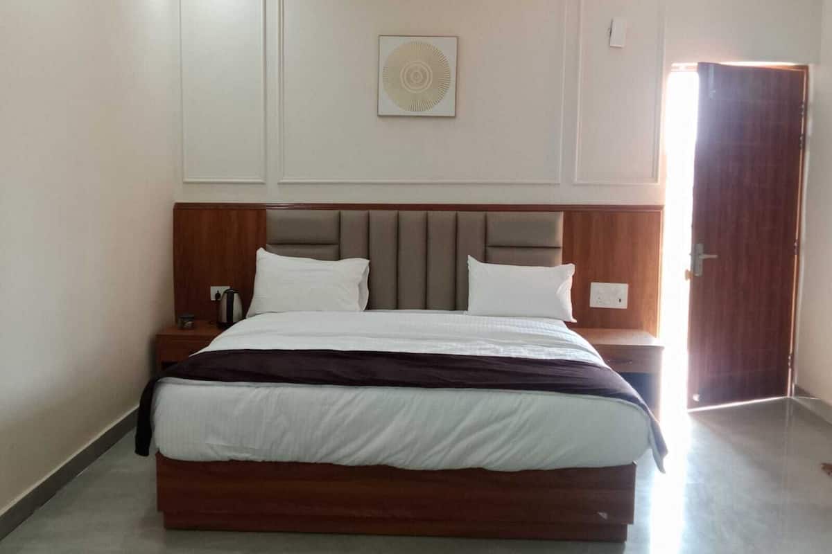 Habitación de hotel con una cama grande, cabecera de madera, paredes blancas, una mesita de noche pequeña y una puerta.