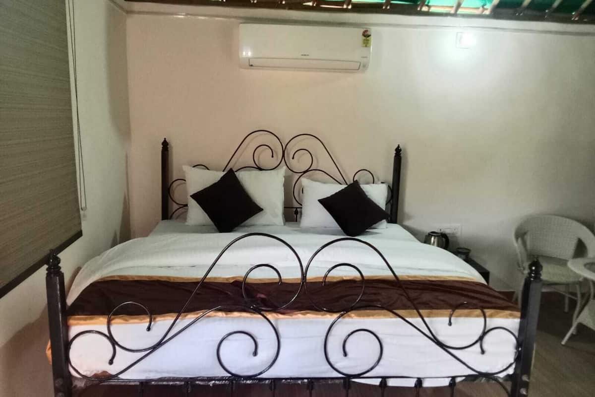 Una cama con estructura metálica, ropa de cama blanca y dos almohadas negras.