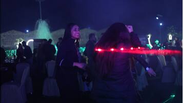 Un grupo de personas bailando en un evento al aire libre, con una fuente y luces decorativas de fondo.
