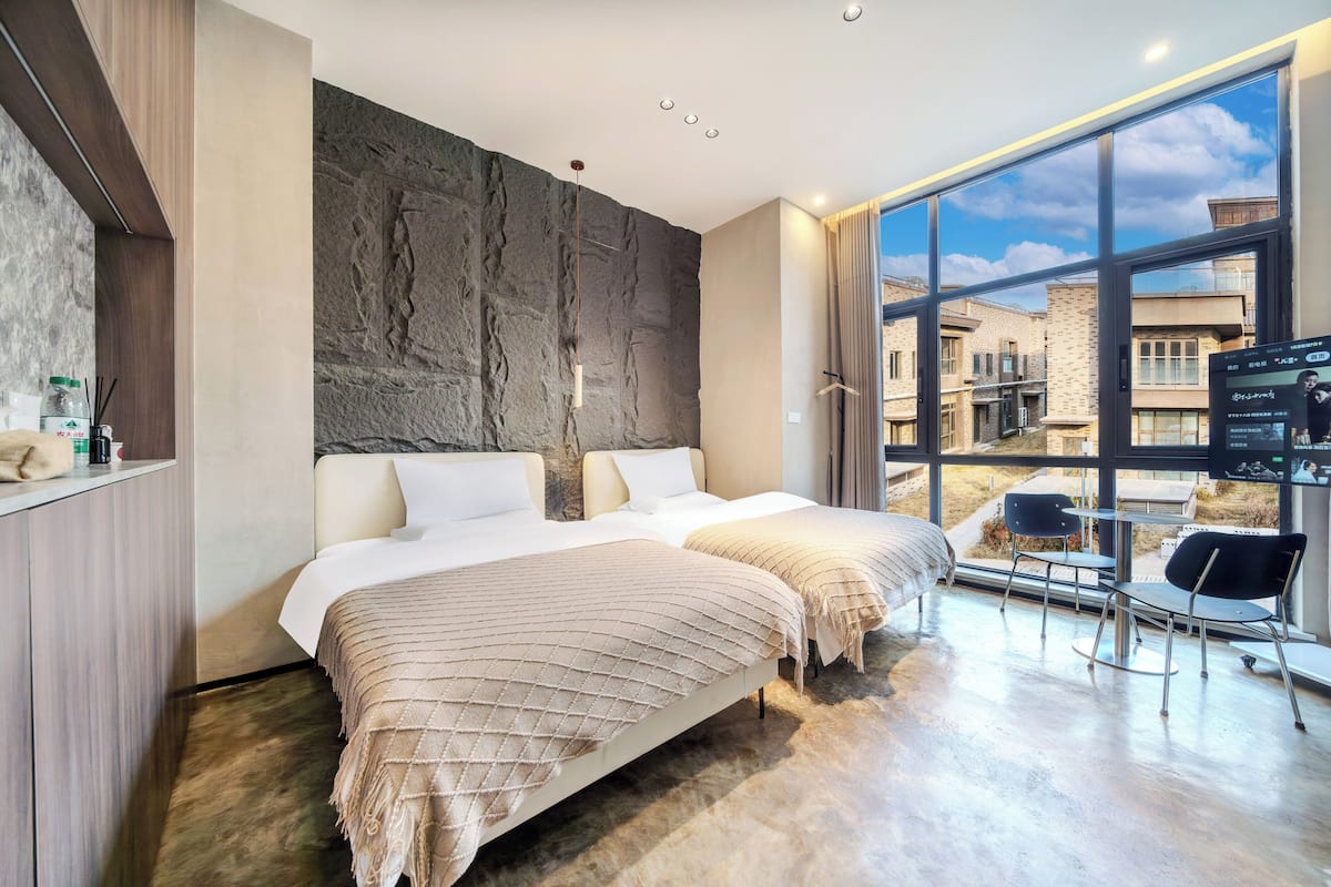 Ein modernes Hotelzimmer mit einem großen Bett, einer Sitzecke mit Tisch und Blick auf die Stadt durch große Fenster.
