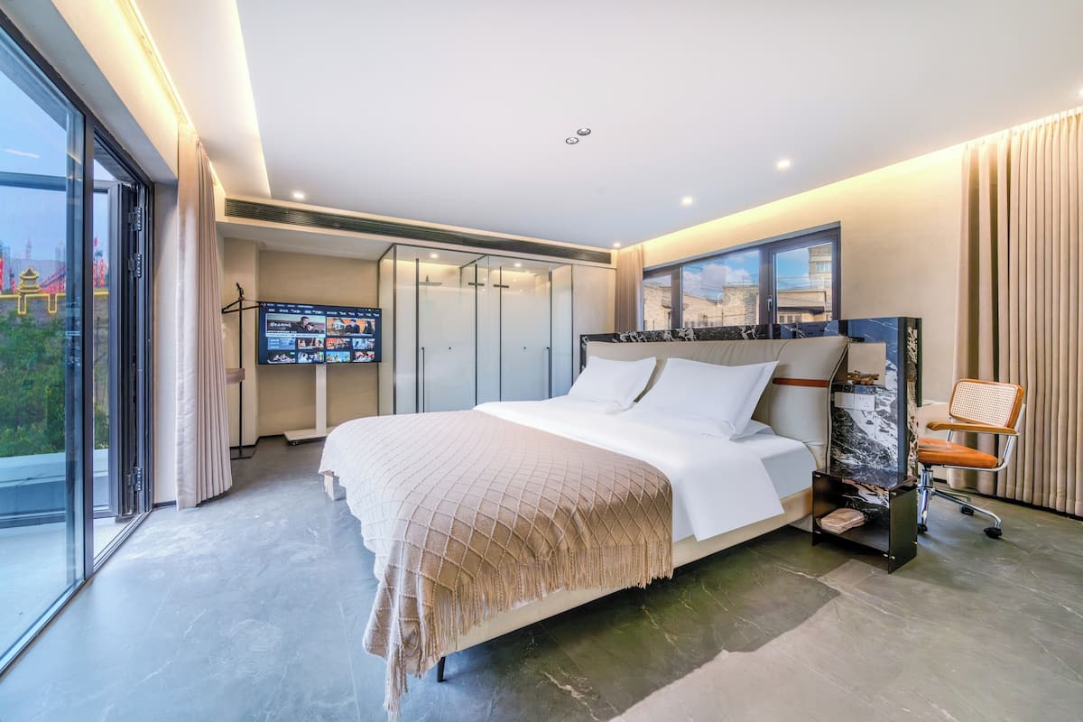 Ein modernes Hotelzimmer mit einem großen Bett, einem Fernseher, einem Kleiderschrank und einem Balkon mit Blick auf die Stadt.