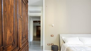 Un dormitorio con un armario de madera, una cama con ropa de cama blanca y un taburete pequeño.