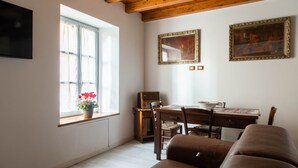 Una sala de estar acogedora con techo de madera, un ventanal con cortinas, una mesa de comedor con sillas y dos cuadros en la pared.