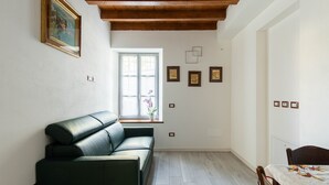 Een kamer met een donkergroene bank, een houten plafond, een raam met uitzicht en een bed met een beddeken met patroon.